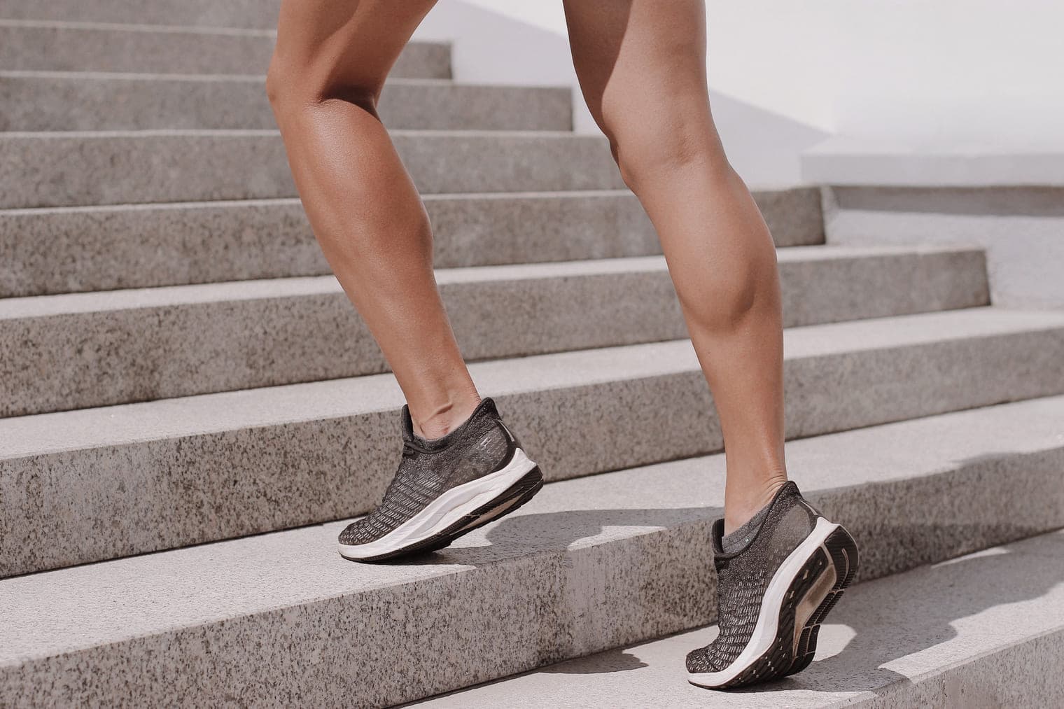 Legs in trainers climbing a flight of concrete stairs.