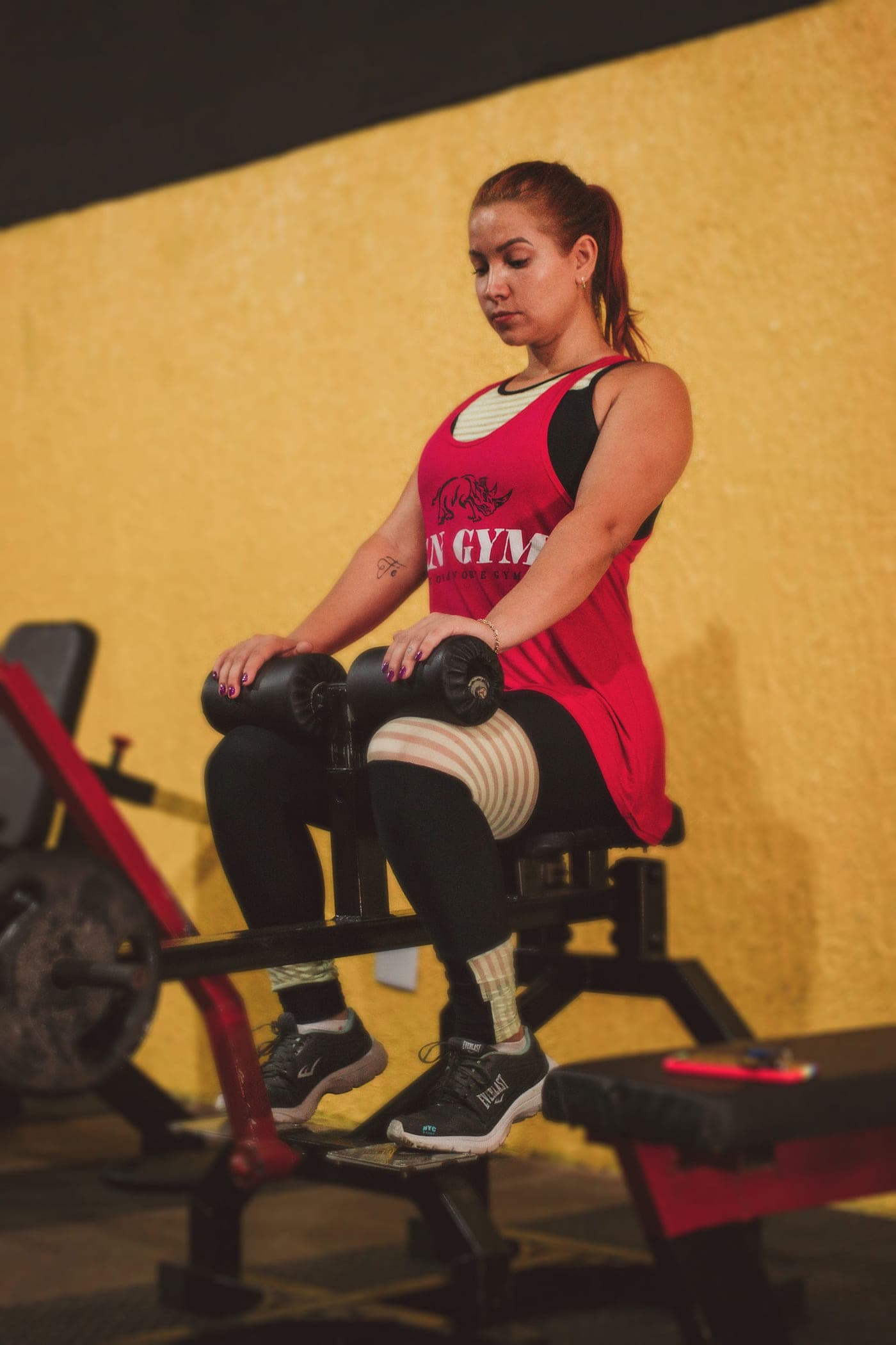 A woman seated at a leg machine against a yellow wall, mid-set with her knees extended.